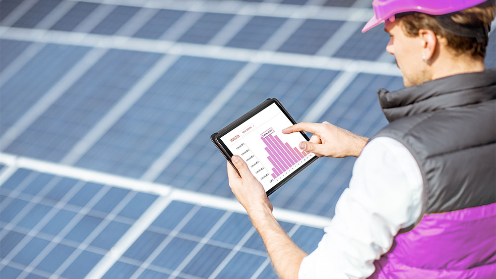 Profissional analisa dados de desempenho solar em tablet sobre painéis fotovoltaicos, representando práticas de gestão energética.