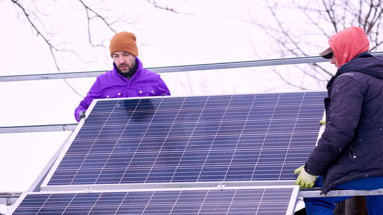 Instalação de placas solares no inverno por técnicos agasalhados, mostrando que o sistema funciona mesmo com frio.